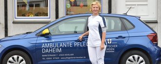 Pflegerin steht vor einem blauen Kleinwagen mit der Aufschrift: "St. Marien - Ambulante Pflege Daheim - Deutscher Orden"